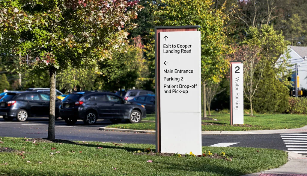 Outdoor vehicular directional sign as well as a Visitor Parking sign in the background.