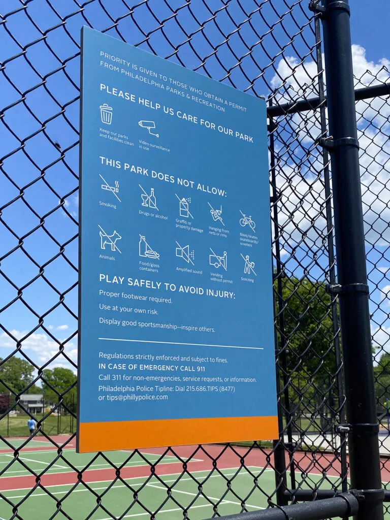 Sign mounted outside tennis court with notices and rules