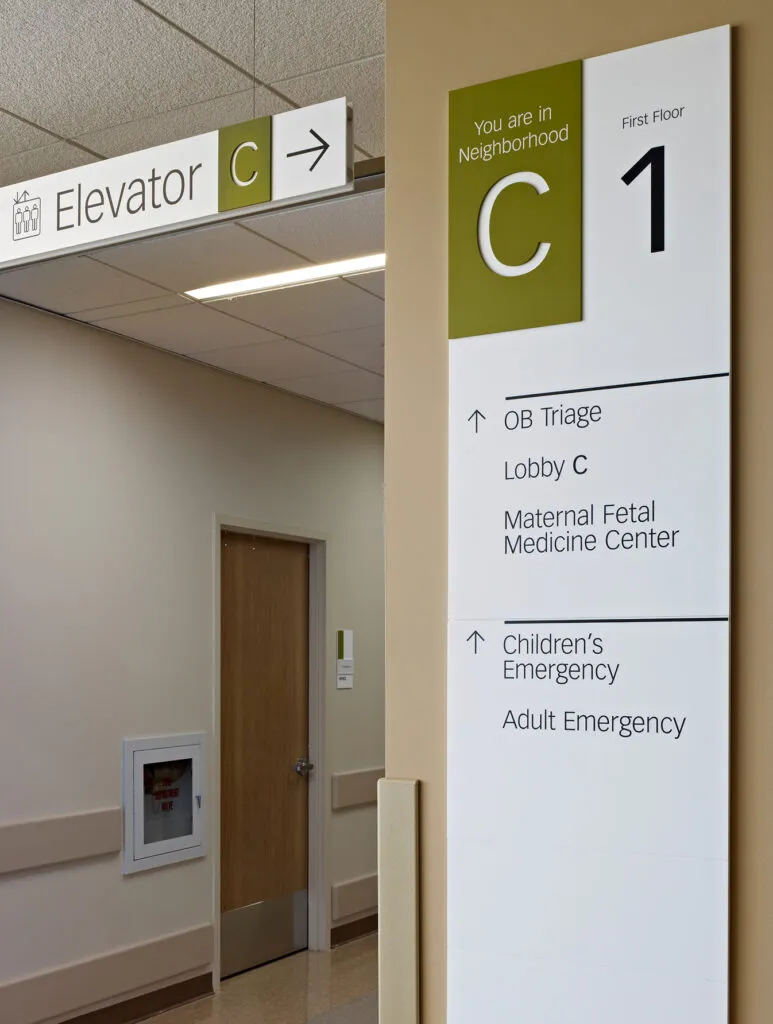 Neighborhood C identification and directional sign with overhead in background identifying the closest elevator