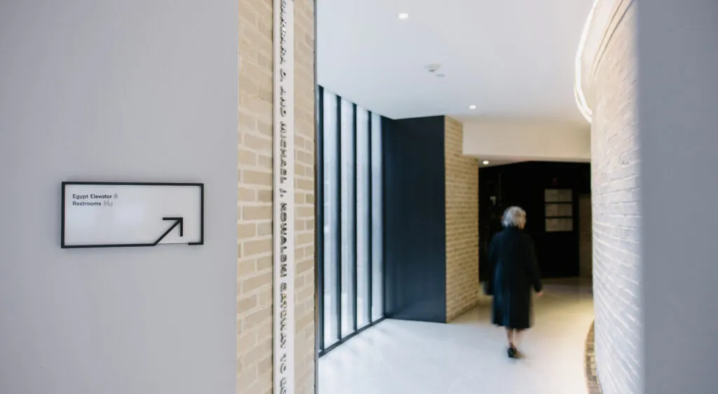A sign directing to the Egypt Elevator and restrooms with an older woman walking further down the hallway