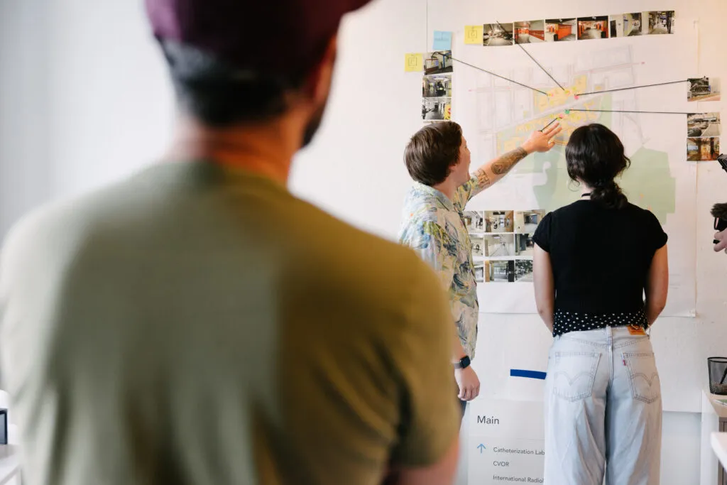 Exit employees looking at map pinned to wall. Map surrounded by images and push pins, string connects ideas on the wall