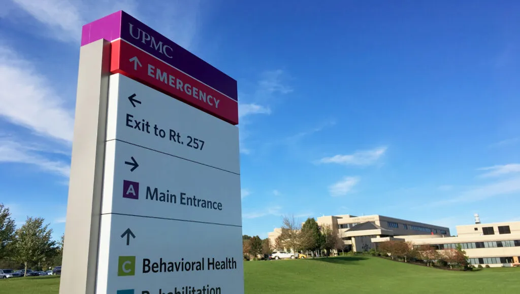 UPMC entrance sign with hospital in the background on the skyline